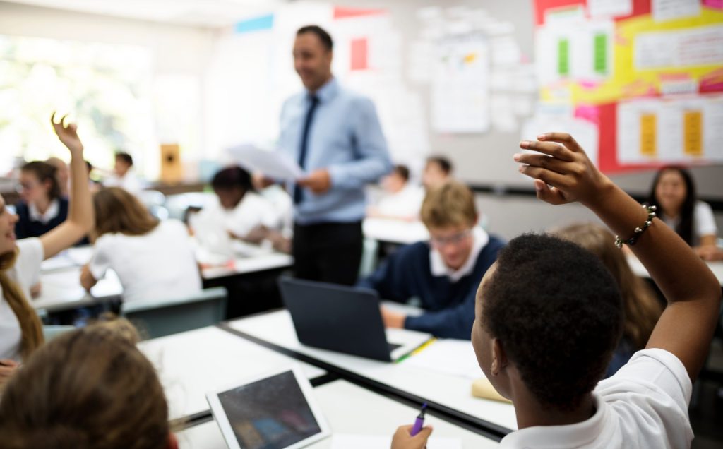 Teacher standing in a classroom with students hands raised